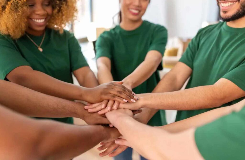 A group of people stand in a circle, smiling, and stacking their hands together in a gesture of teamwork and unity.