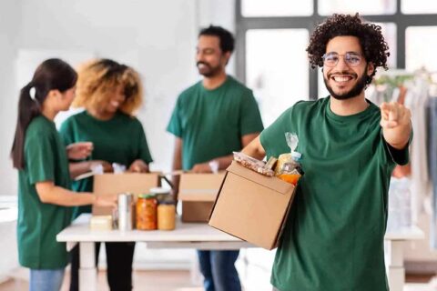 A cheerful group wearing green shirts packs food items into boxes