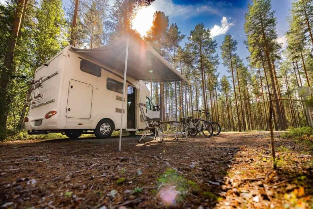 A camper van with an awning is set up in a sunlit forest