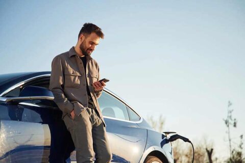 A man in casual attire leans on a charging blue electric car