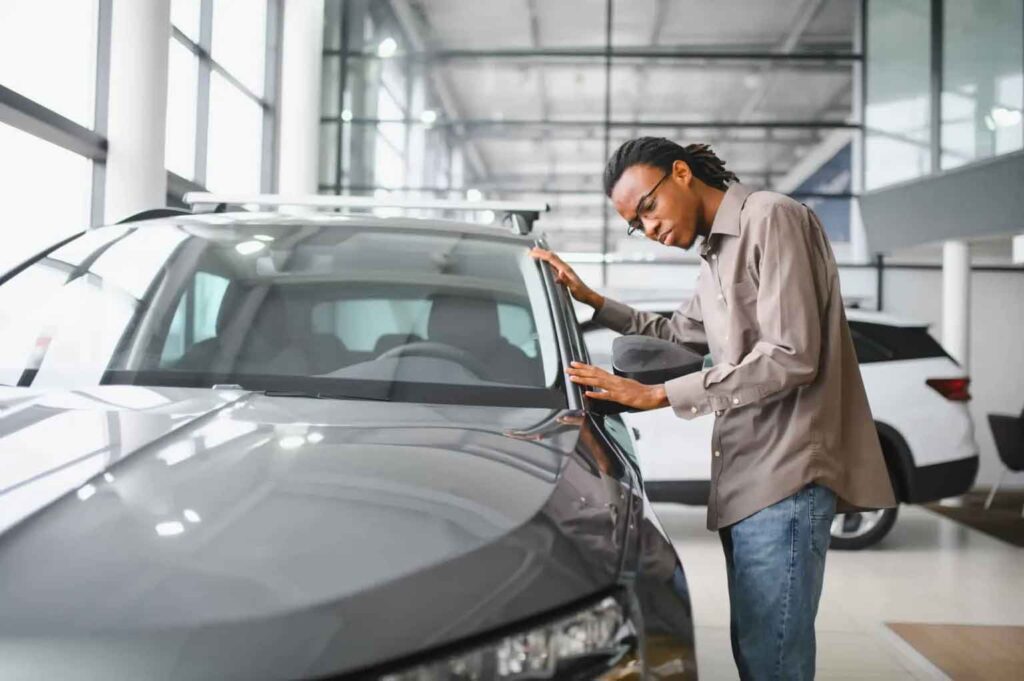 A man examines a sleek, gray car's exterior in a bright, modern showroom. 