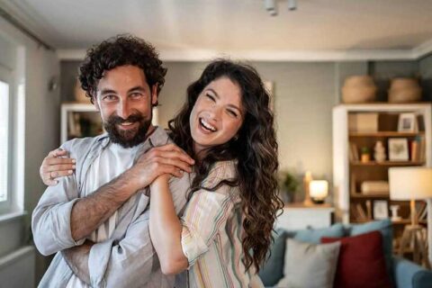 A happy couple embraces and laughs in a cozy living room.