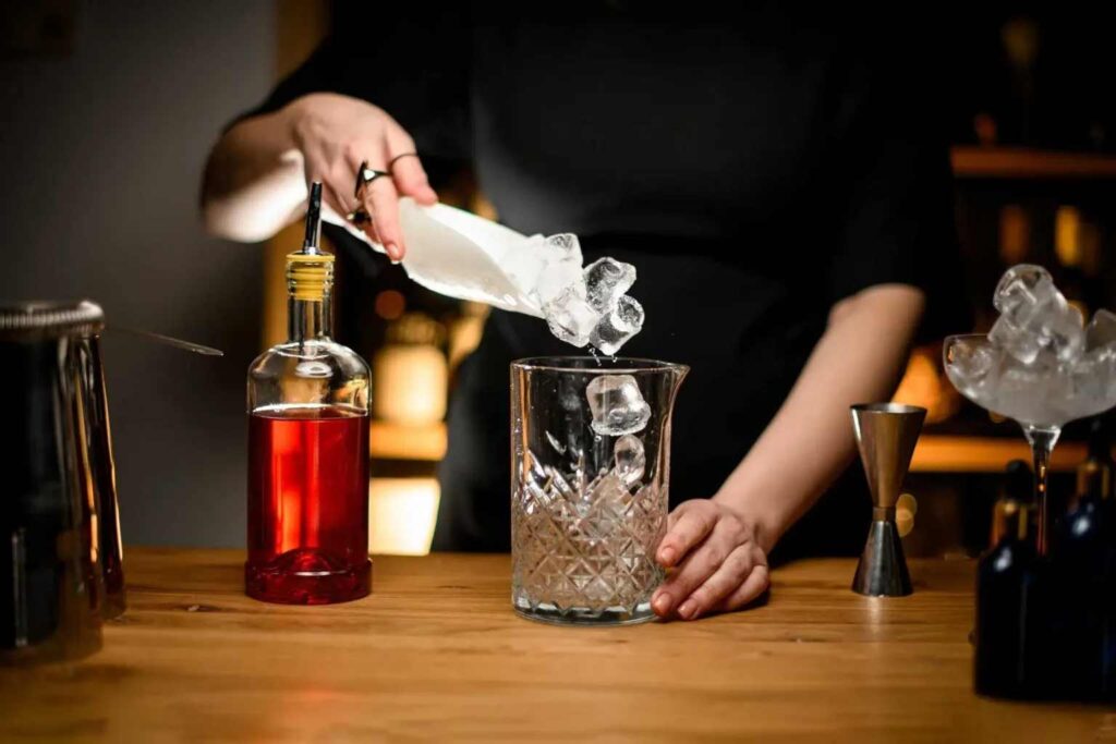 Bartender adding ice to a glass at a wooden bar.