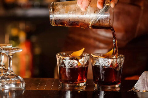 Bartender pours dark liquid into two glasses