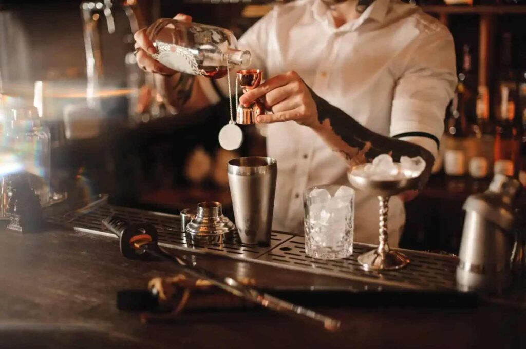 Bartender in a white shirt pours liquor into a jigger,