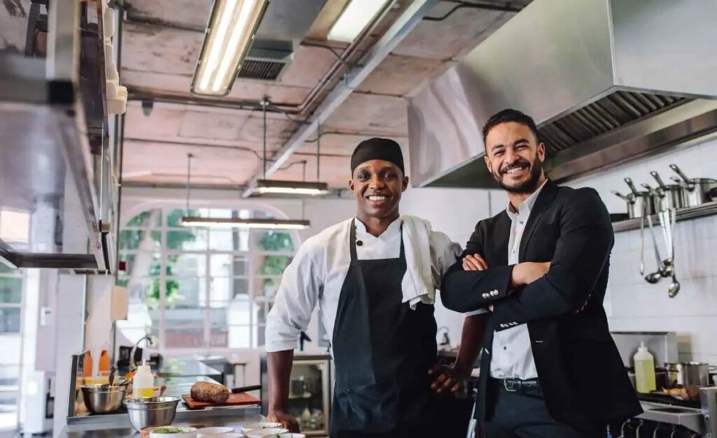 Chef and businessperson smiling in a modern kitchen.